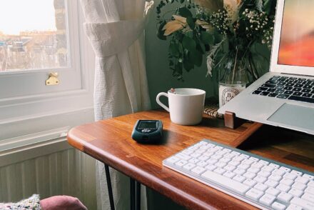 A desk featuring a laptop and working from home scene including flowers, a mug and an Omnipod PDM