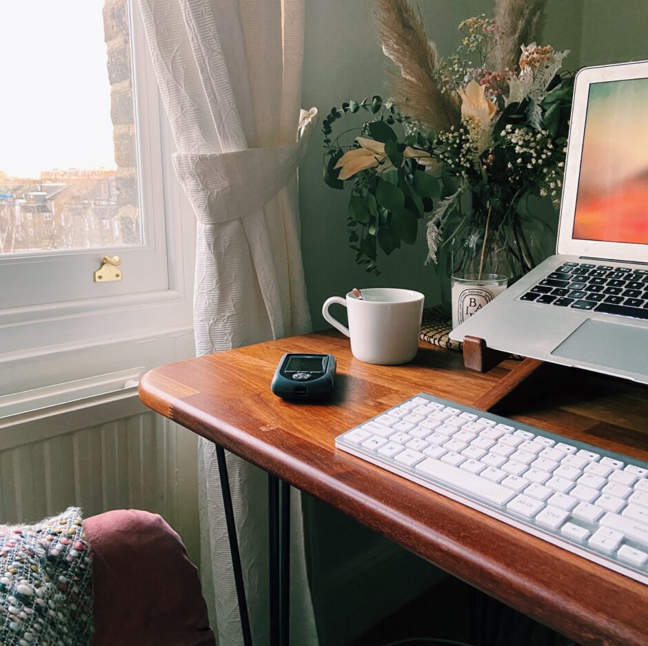 A desk featuring a laptop and working from home scene including flowers, a mug and an Omnipod PDM