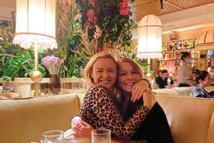 Two type 1 diabetic females hugging and smiling at a restaurant table with flowers in the background