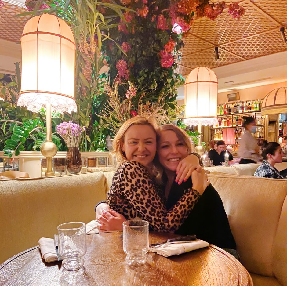 Two type 1 diabetic females hugging and smiling at a restaurant table with flowers in the background