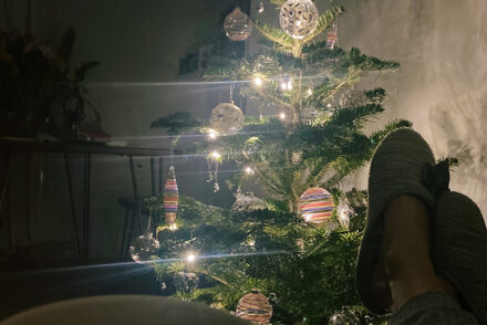 Two feet in slippers propped up in front of a glowing christmas tree in a living room