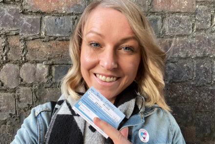 Woman smiling holding up a pfizer covid vaccine card