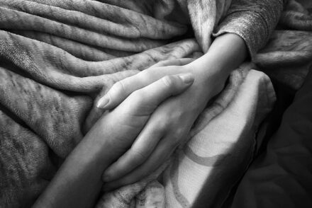 A close up of a hand holding the hand of a person who is laying in a bed